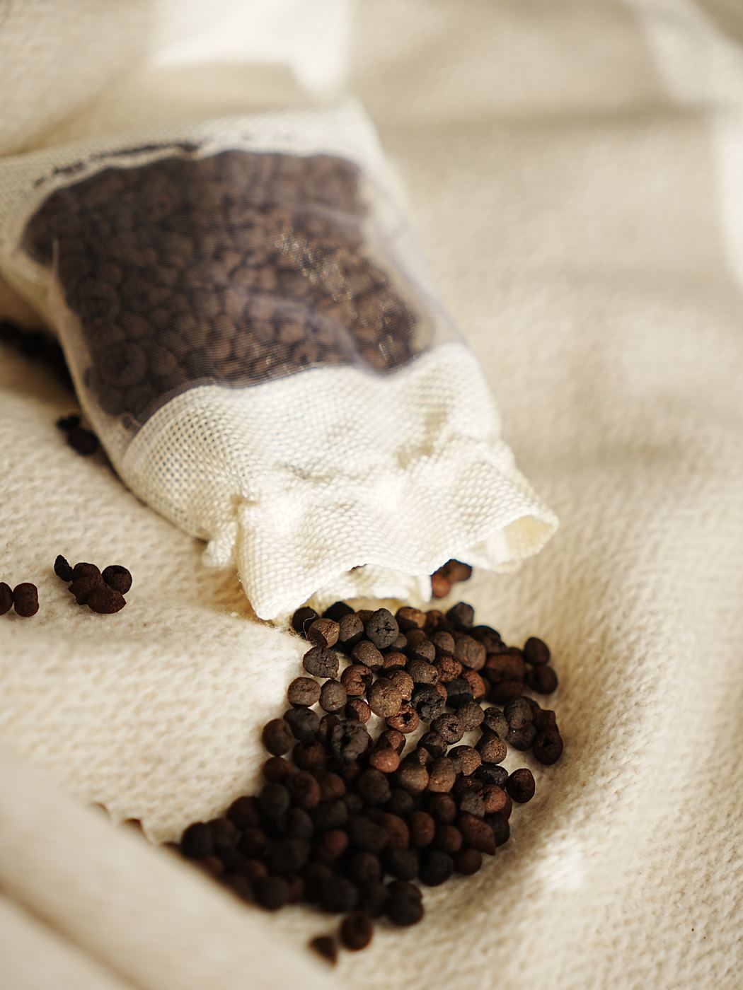 Coffee-ground pellets spilling out of a breathable fabric bag onto linen